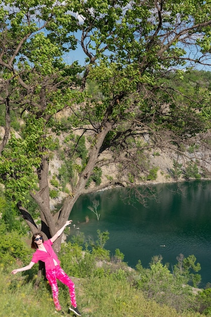Landscape girl in pink near the tree against the backdrop of mountains and lake