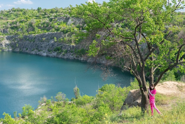 Landscape girl in pink near the tree against the backdrop of mountains and lake