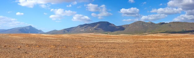 Landscape of harvested farm land on a cloudy day empty wheat field against a blue sky rural agriculture with dry pasture near mountains wide angle of empty dirt country for copy space background