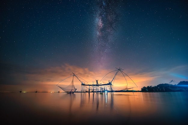 Landscape image of milky way over traditional square fishnet equipment at Pakpra Canal, Phatthalung, Thailand