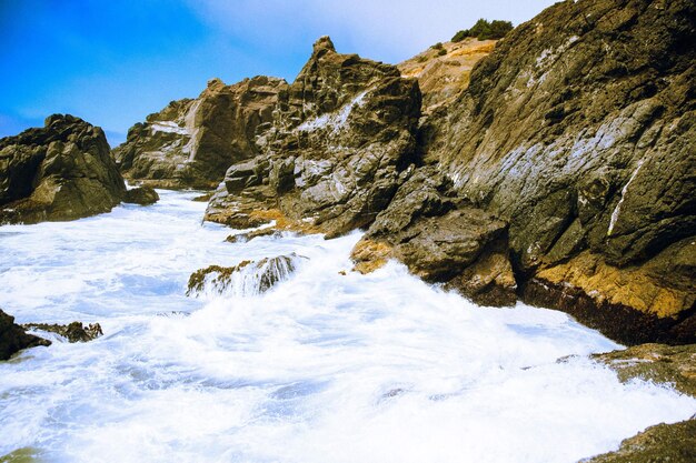 Photo landscape of ocean waves touching rock mountains