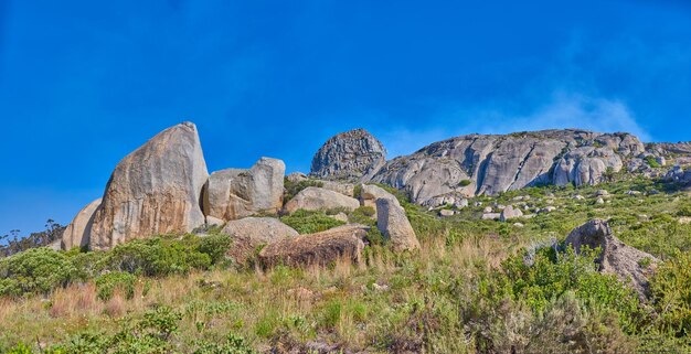 Landscape of rocky mountain with boulders against a blue sky in summer Green field with rocks and wild grass growing on sunny day outside with copy space Scenic remote travel destination in nature