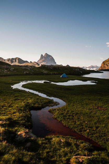 Landscape at sunset with a winding river and a tent on the meadows and with a view of the Midi
