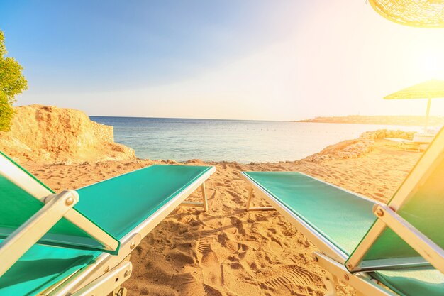 The landscape of two beachchairs on the sand near sea