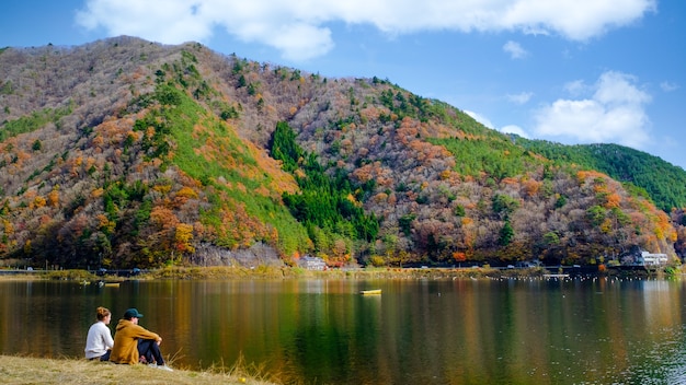 写真 河口湖の紅葉と日本の川沿いに座っているカップルの風景を見る