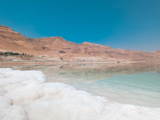 Landscape view on Dead Sea salt crystals formations clear cyan green water and mountains at Ein Bokek beach Israel