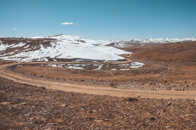 Landscape view of a winding dirt road along snow capped mountain range, pakistan.