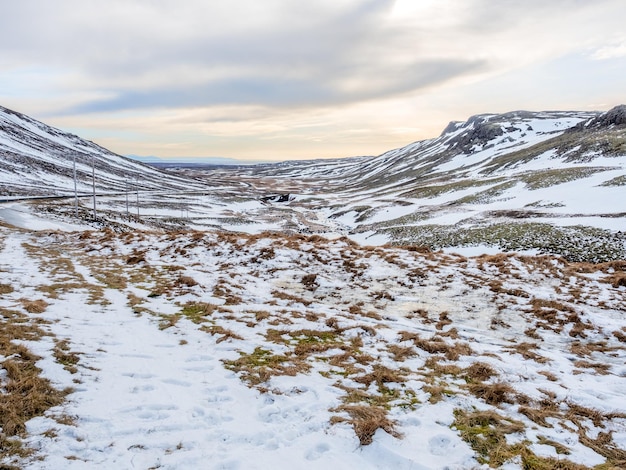 アイスランドの道路脇に沿って曇り空の下で冬の雪と風景の景色