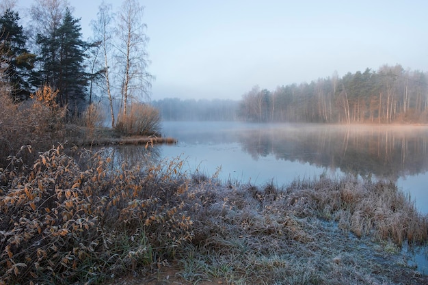 Landscape with first frost on a forest blue misty lake with beautiful birches autumn colorful landscape on a bright morning