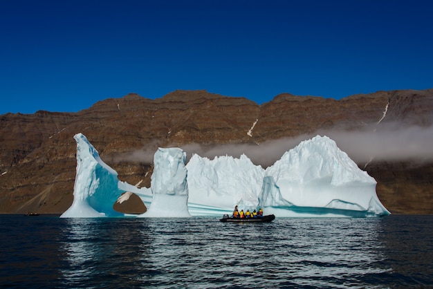 Landscape with iceberg in Greenland at summer time. Sunny weather. Inflatable boat with tourists.