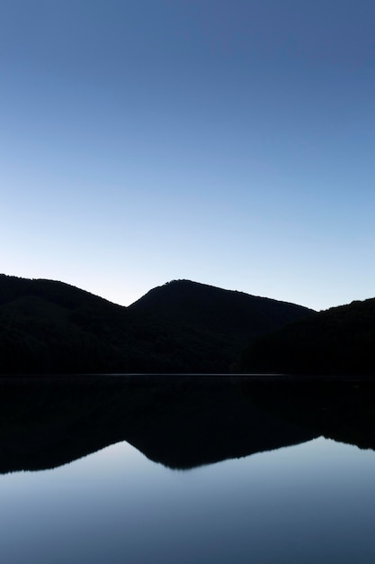 Landscape with mountain reflected in the water of a lake. Clear sky. Shade of blue. Space for text.