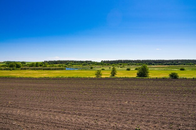 Landscape with plowed field with black soil on the background of green banks and river