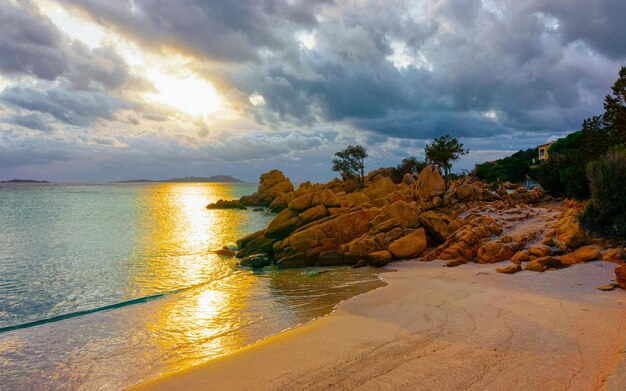 이탈리아 사르데냐 섬의 지중해 코스타 스메랄다(Costa Smeralda)에 있는 카프리치올리 해변(Capriccioli Beach)에서 낭만적인 일몰이 있는 풍경. 구름과 하늘입니다. Porto Cervo와 Olbia 지방. 혼합 매체.