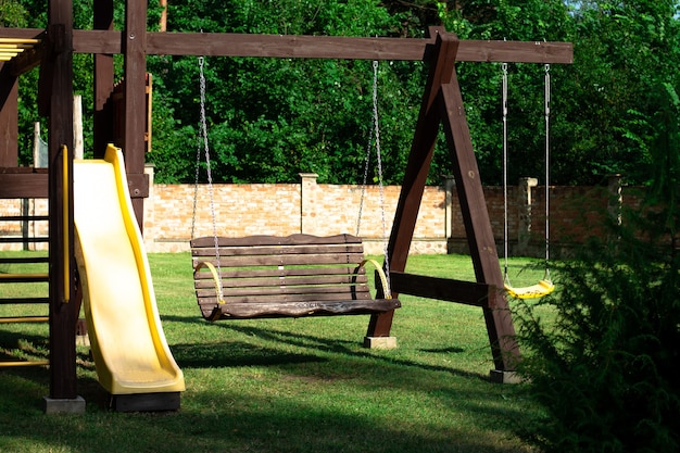 Landscape. Wooden playground with swings, slide and stairs on the background of a brick fence in the courtyard of private house.