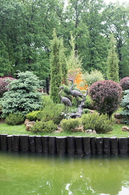 Landscaping in the park, many different plants, a lake and a statue of storks