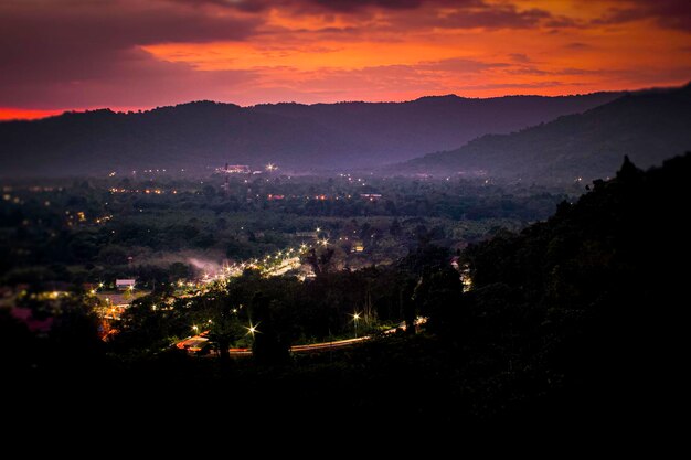 Landschap met alpine bergvallei lage wolken bos paarse lucht met sterren stadsverlichting bij zonsondergang Luchtfoto