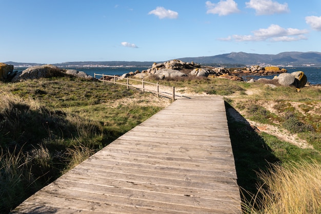 Landschap met een houten gang die een wild strand met zand en vegetatie kruist. Illa de Arousa, Pontevedra, Spanje