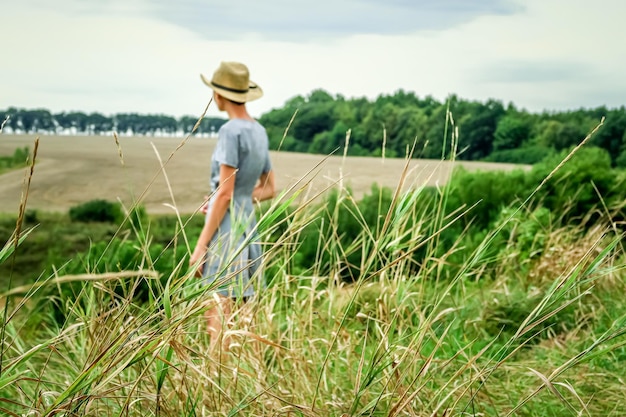 landschap met glooiende korenvelden, bos, gras op de voorgrond en een vrouw onscherp