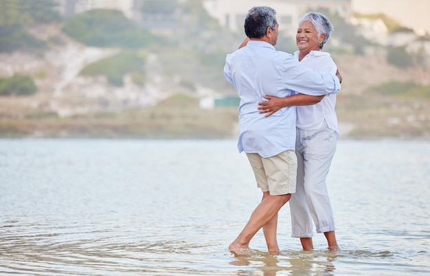 Landschap strand en dans van een senior paar glimlachend en dansen in het zee- of oceaanwater en knuffelen bij zonsondergang Gelukkige glimlach of binding van een oude man en vrouw dansen in de natuur voor huwelijk