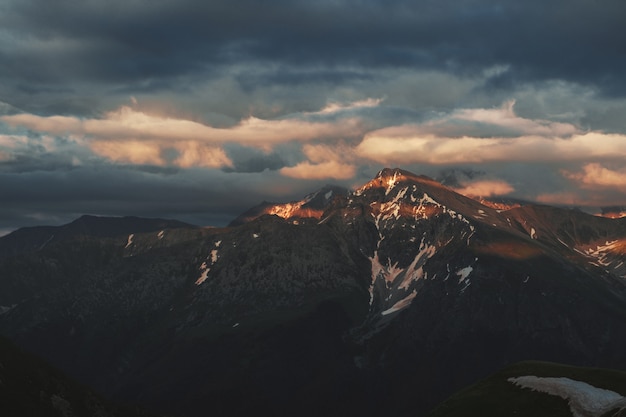 Foto landschap van de berg het piekzonsondergang met sombere dramatische hoofdzakelijk bewolkte hemel en oranje en rode zonstralen