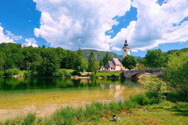 Landschap van de kerk van Saint John Baptist op het Bohinj-meer in Slovenië. Natuur in Slovenië. Uitzicht op blauwe lucht met wolken. Prachtig landschap in de zomer. Alpine reisbestemming. Julische Alpen bergen