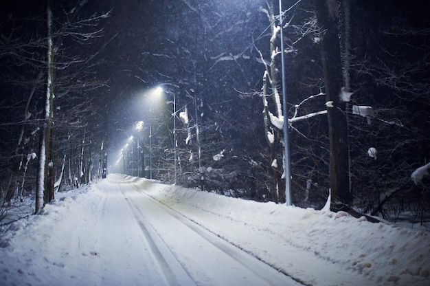 Landschap van de lege weg van de nachtwinter die door sneeuw wordt behandeld.