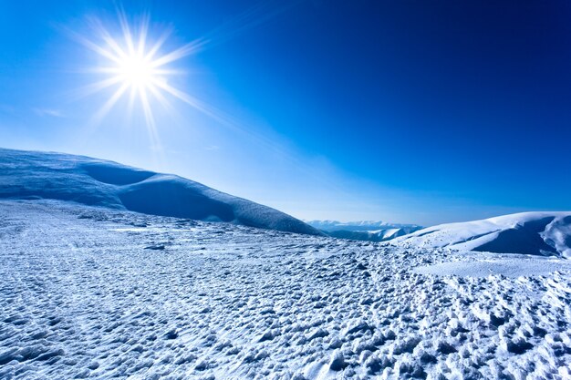 Landschap van de vallei van de sneeuwwinter en de bergen en de zon in hierboven op duidelijke ijzige winterdag