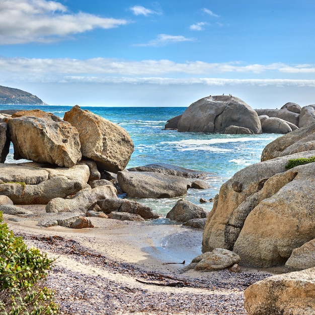 Landschap van prachtige grote rotsblokken in de oceaan met een blauwe bewolkte hemel Rots- of granietstructuren die onder de zon schijnen in de buurt van kalme schuimende golven op een populaire strandlocatie Kaapstad Zuid-Afrika