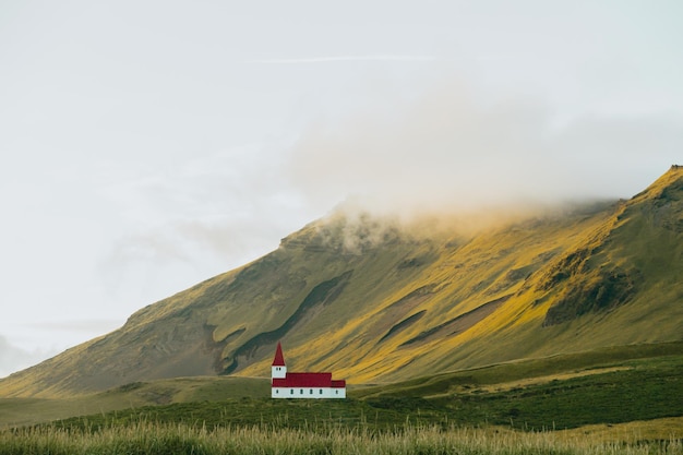 Landschapsbehang van de kerk van Vik i Myrdal in IJsland voor een enorme berg tijdens de zonsondergang Kopieer de ruimteafbeelding humeurige stijl Bezoek de reisroute van IJsland op woestenijen