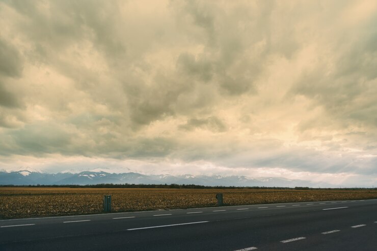 Landschapsfoto met een deel van weg, tarwe en montains op een bewolkte dag.