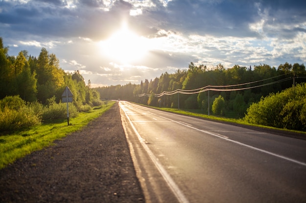 Landweg met markeringen midden in het bos. Pad en voorwaartse beweging in de zon. Mooi, groen bos in het voorjaar bij zonsondergang. Concept voor succes in het toekomstige doel en het verstrijken van de tijd