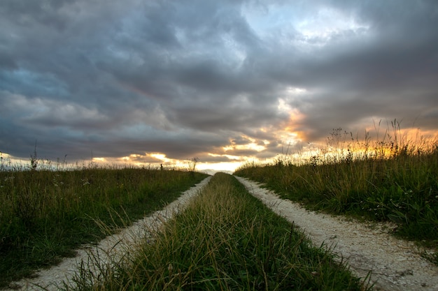 Landweg onder donkere velden bij zonsondergang met dramatische cloudscape.