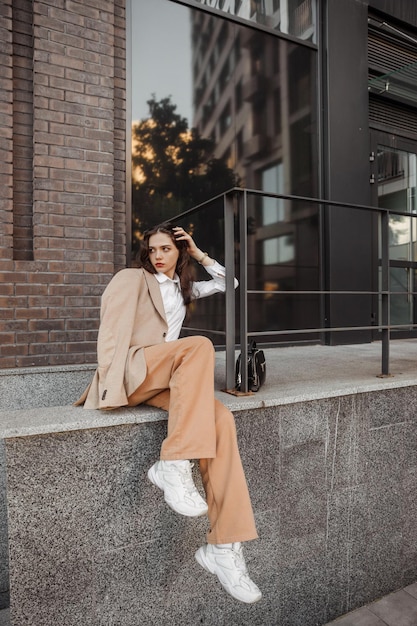 lang stijlvol meisje met oversized jas poseren in de buurt van de reling en trappen op de achtergrond van de stad
