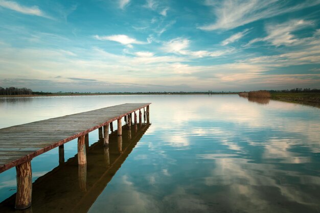 Foto lange houten brug op de horizon van het meer en witte wolken op de blauwe hemel