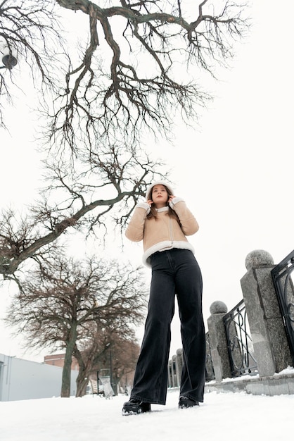 Lange jonge slanke vrouw in zwarte broek en beige schapenvacht jas in snowcovered park Stijlvol meisje Verticaal frame