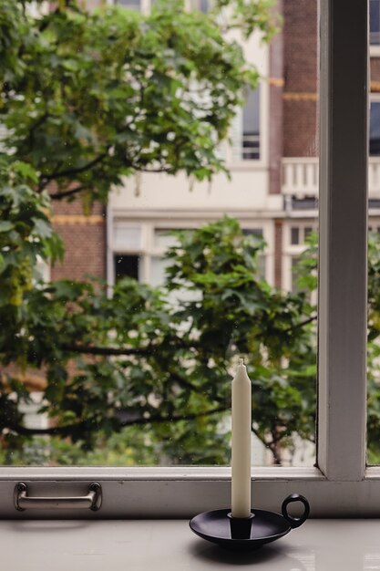 Lange witte kaars in een vintage kandelaar in oude stijl die op het houten grote raam staat