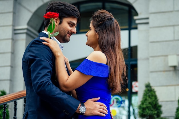 Langharige brunette Indiase vrouw in blauwe jurk met haar knappe vriendje dating .man geeft roos aan zijn vriendin in de zomer downtown straat.