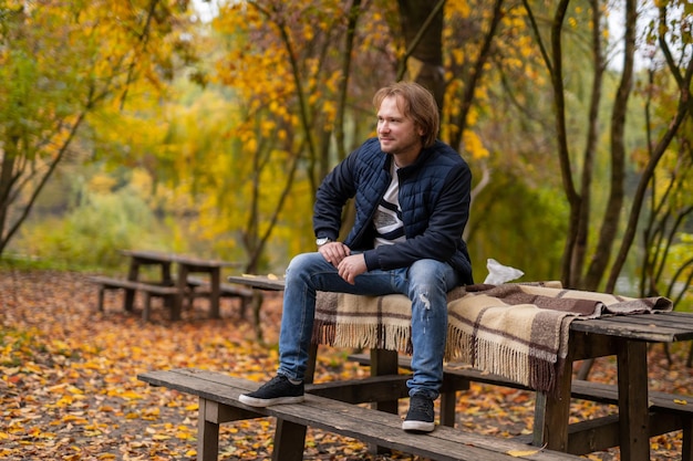 Langharige man zit op een bankje in het park. Gouden herfst en zonnige dagen. Portret van een knappe man.