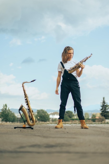 Langharige saxofonist in zwarte overall poserend met zijn muziekinstrumenten