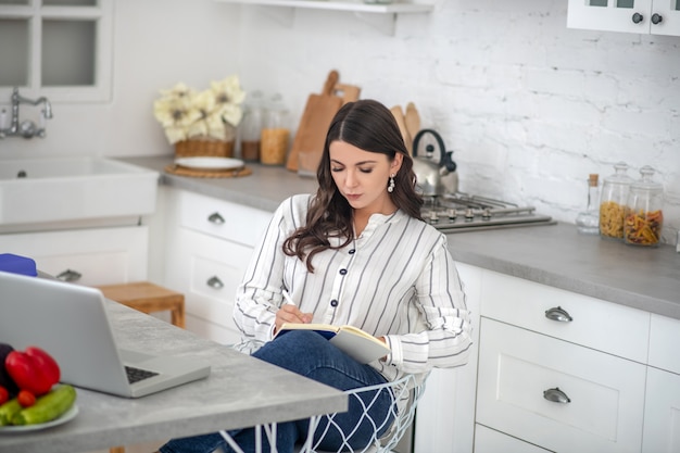 Langharige vrouw in een gestreepte blouse aan de tafel zitten en lezen