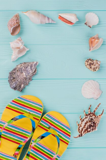 Langs de omtrek zijn verschillende zeeschelpen en heldere sandalen in de hoek op een turquoise achtergrond. Kopieer de ruimte in het midden.