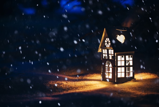 Lantern house with burning candle on snow in the evening.