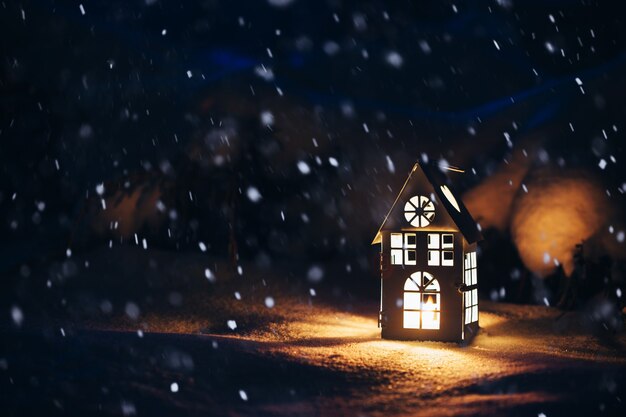 Lantern house with burning candle on snow in the evening.