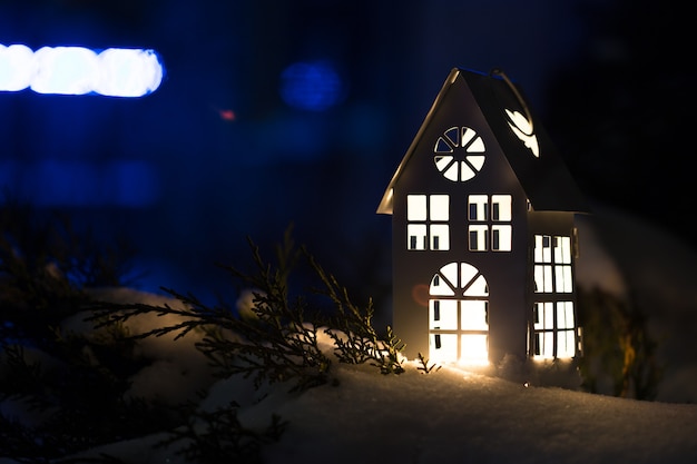 Lantern house with burning candle on snow in the evening.