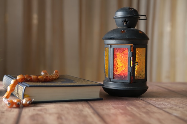 Lantern light holy book quran and rosary on table close up