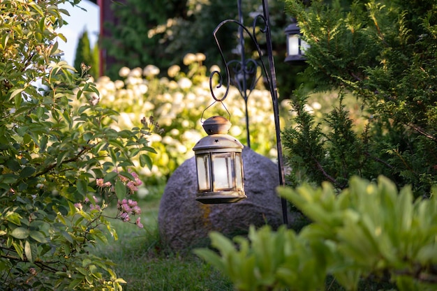 a lantern sits in a garden with a red house in the background.