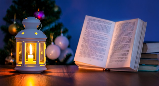 Lantern with book and open book near Christmas tree. Reading in candle light_