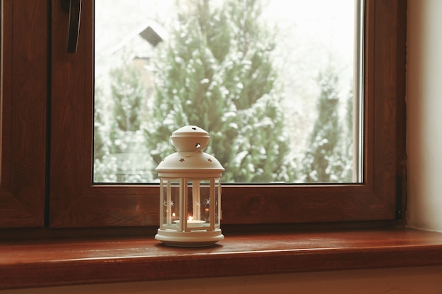 Lantern with burning candle on wooden windowsill