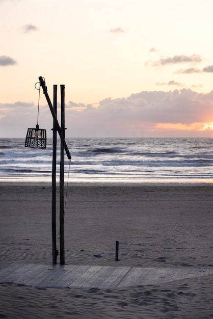 Lantern with wicker lampshade on a double wooden pole and crossbar on the seashore