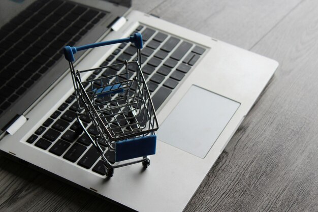 Фото Ноутбук и мини-тележка для покупок на деревянном столе концепция онлайн-покупок